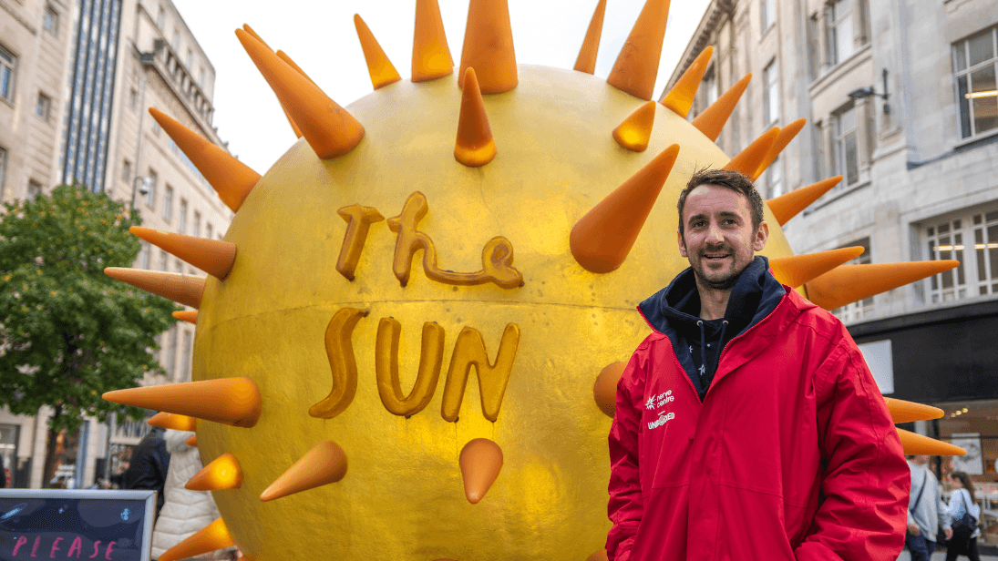 A man standing beside a sculpture of the sun 
