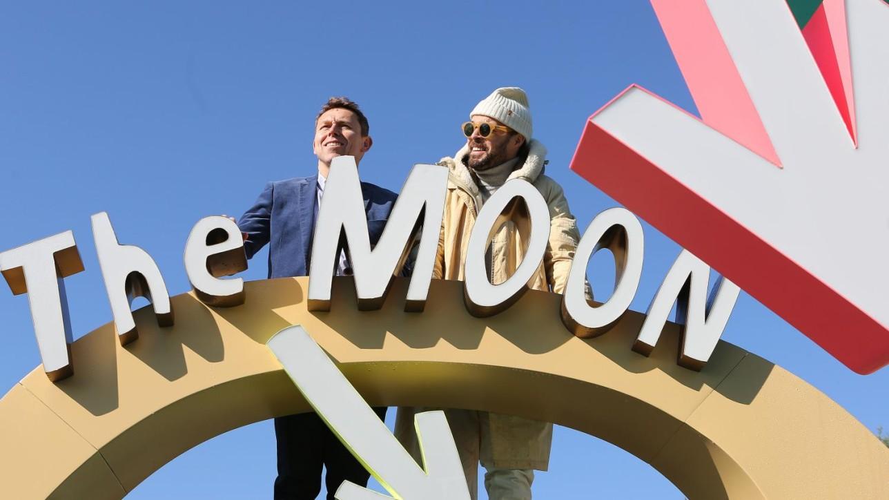 Two people standing next to The Moon sculpture