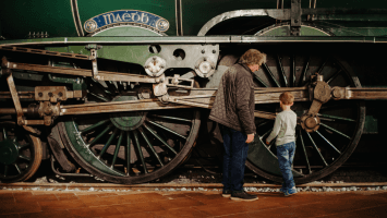 An older man with a young boy standing beside a large green train 
